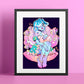 A framed art print featuring a colorful cartoon-style illustration of a woman in a shell with fish, displayed against a pink background.