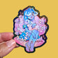 Colorful sticker of a fantasy character held by a hand on a yellow background
