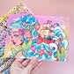 Colorful illustration of a mermaid and ship on a card held by a hand, with art supplies in the background.